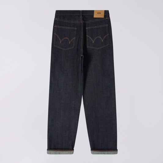 Back view of dark indigo denim jeans with rolled cuffs, showing the back pockets with contrast stitching and a tan leather brand patch at the waistband, photographed on a light gray background.
